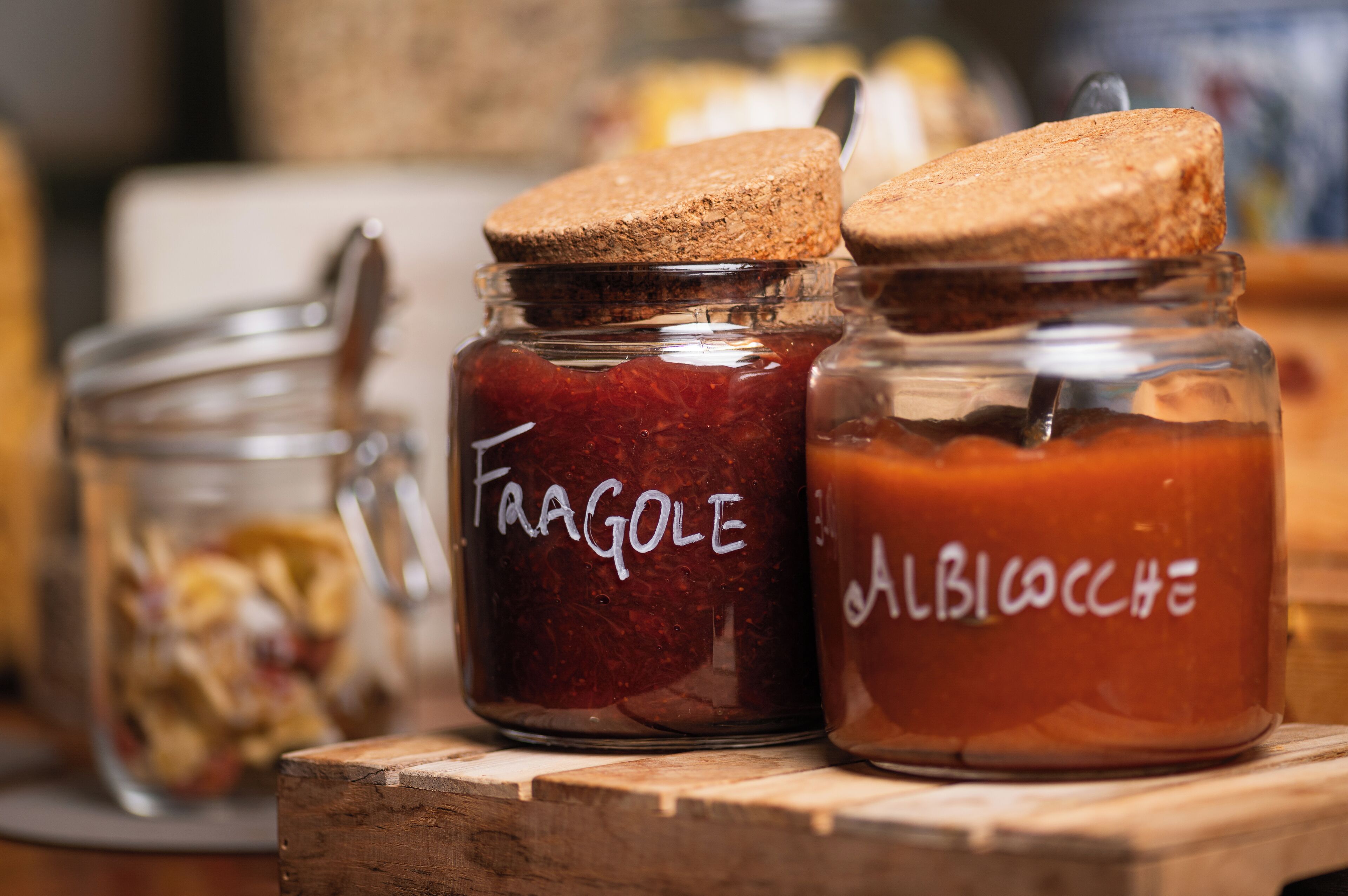 Drei Glasbehälter mit Korkverschluss, beschriftet mit 'Fragole', 'Albicocche' und einem undeutlichen Etikett.