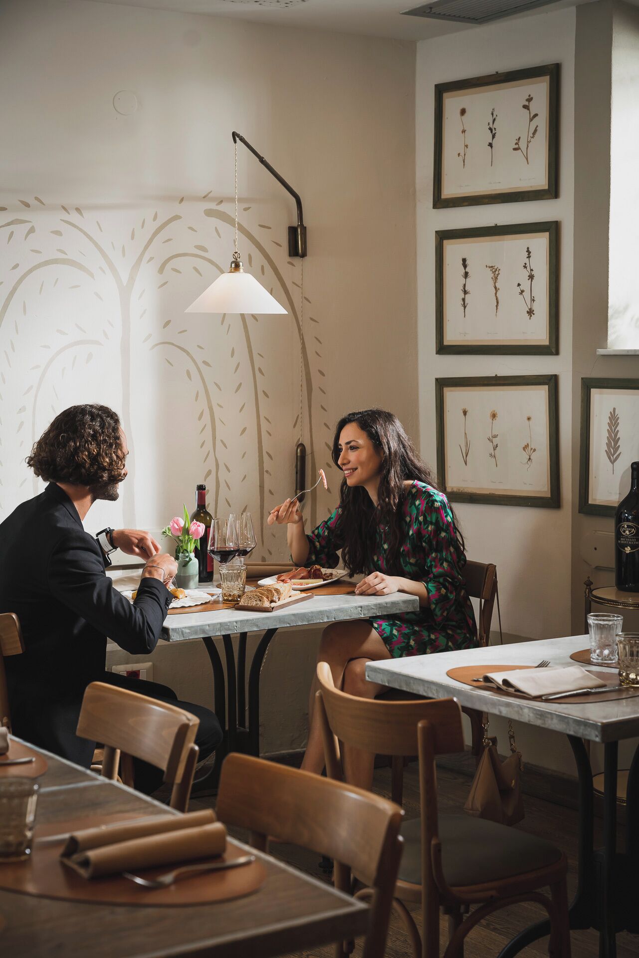 Un comedor con una mesa preparada para dos, con una botella de vino, copas y un florero con flores.
