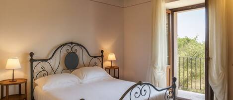 A bedroom with a bed, two bedside tables, and a balcony with curtains.