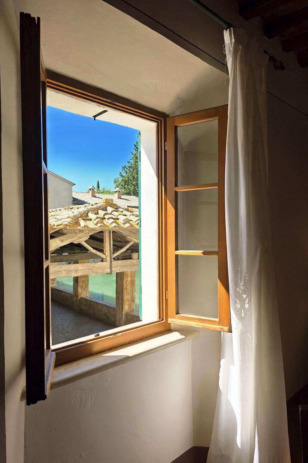 A room with a window overlooking a courtyard with stone walls and a pool.
