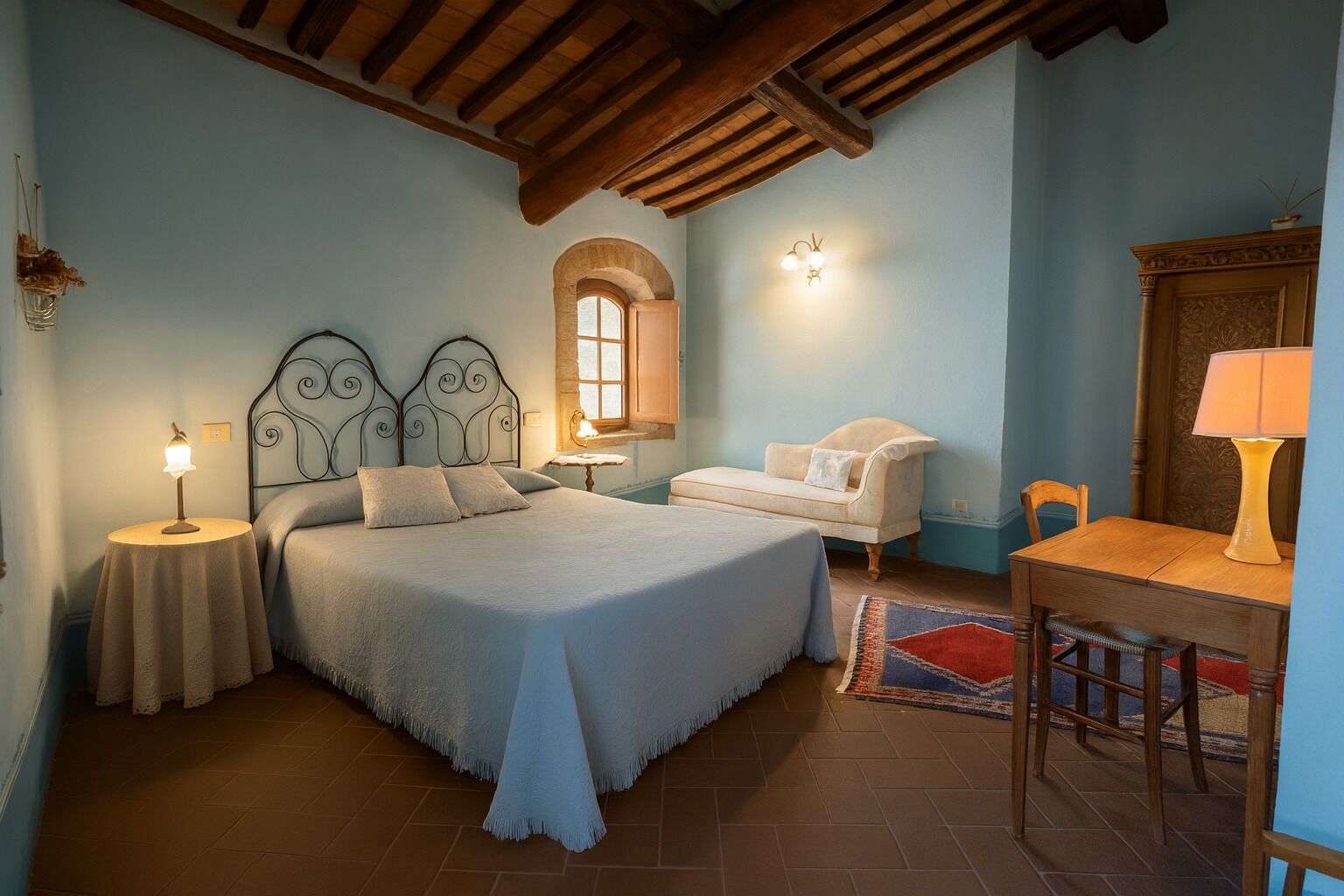 A bedroom with a bed, bedside tables, a chair, a table, a lamp, and a window.