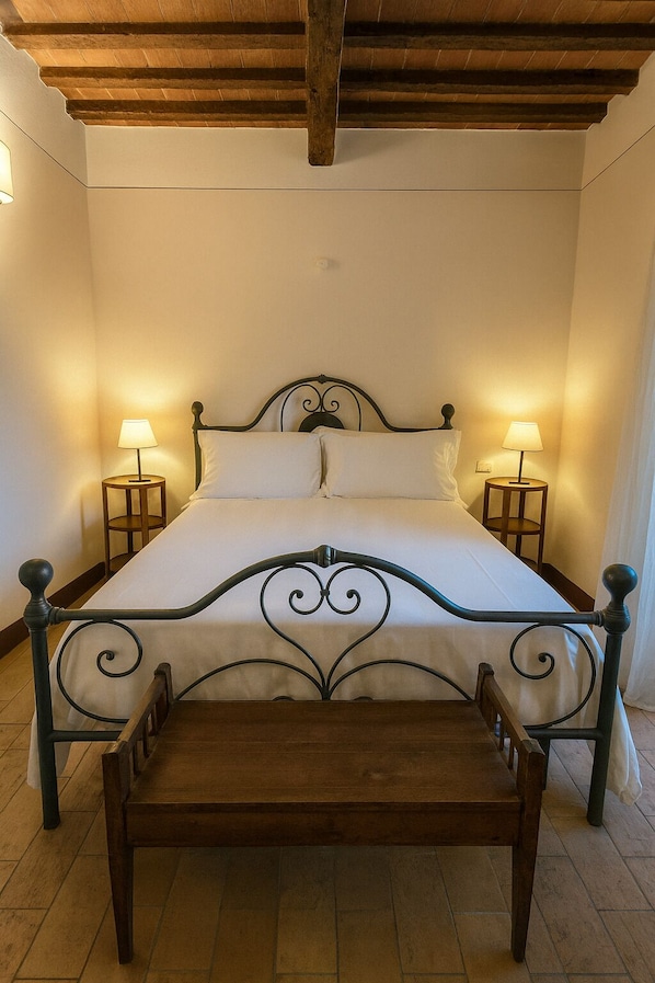 A bed with a metal frame and wooden headboard, flanked by two bedside tables with lamps, in a room with wooden flooring and a sloped ceiling. - L'Orto delle Terme (San Quirico d'Orcia)