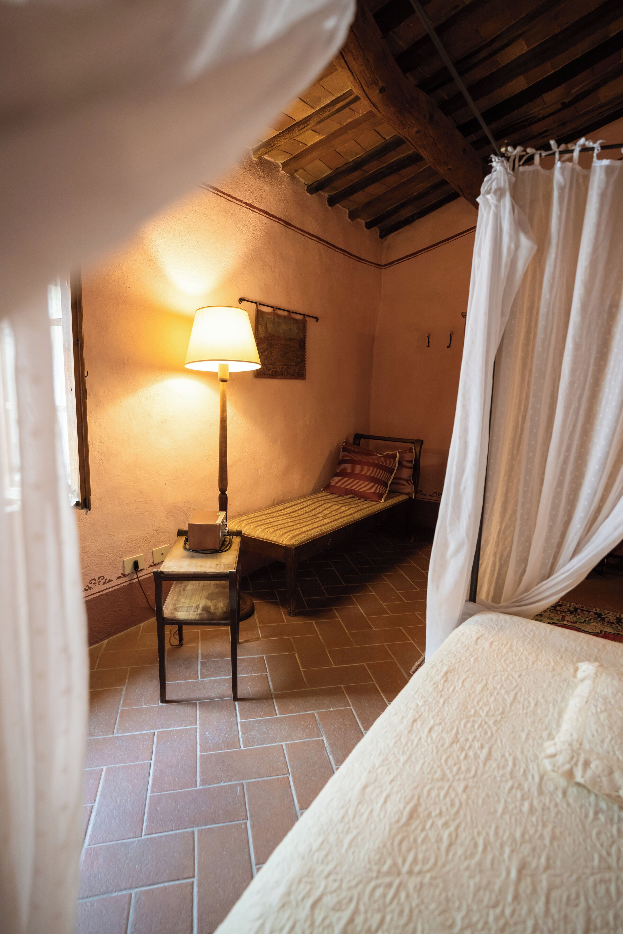A small, cozy room with a bed, a bedside table, a lamp, and a window.