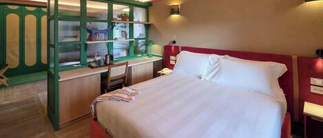 A bedroom with a large bed, a desk with a chair, and a green cabinet with shelves.