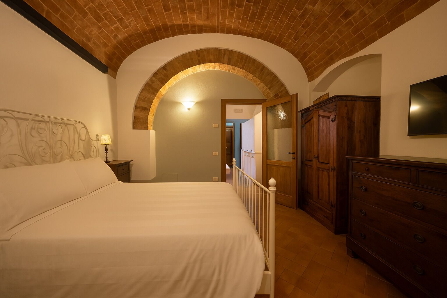 Ein Schlafzimmer mit einem großen Bett, einer Holzkommode, einem an der Wand befestigten Fernseher und einer gewölbten Ziegeldecke.