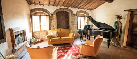 A cozy living room with a yellow sofa, two armchairs, a red rug, a grand piano, and a fireplace.