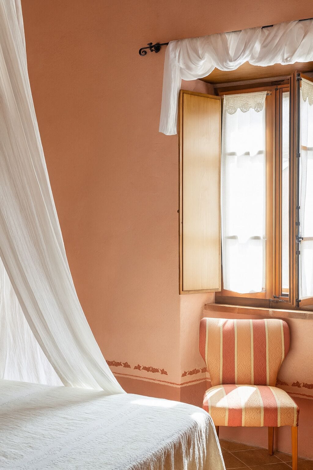 Ein Schlafzimmer mit einem Bett, einem Fenster mit Vorhängen, einem Sessel und einer Wand mit dekorativer Bordüre.