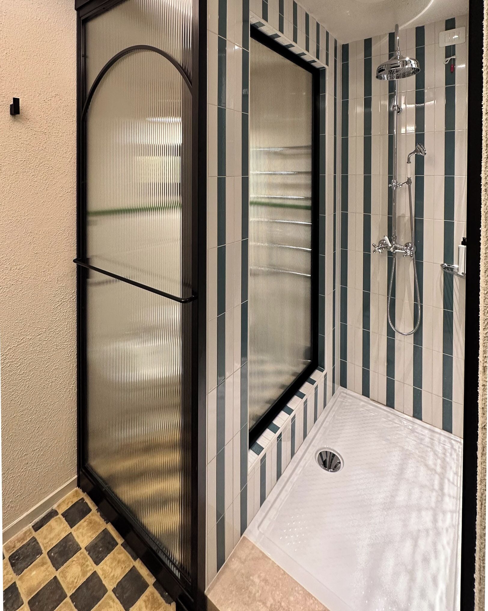 Ein Badezimmer mit Glastür, einer Dusche inklusive Handbrause und gestreiften Fliesen.