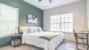 A bedroom with a bed, a desk, and a chair. There are two windows and a ceiling fan. - Boulevard Stays Peaceful 1BR King Suite Pool, Parking Gym 02 (Austin)