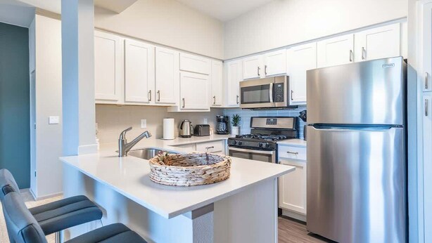 A modern kitchen with white cabinets, stainless steel appliances, and a central island with seating. - Boulevard Stays Tranquil 1BR King Suite Pool, Parking Gym 04 (Austin)