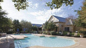 A swimming pool with a deck area, surrounded by lounge chairs and umbrellas, with a building in the background. - Boulevard Stays Tranquil 1BR King Suite Pool, Parking Gym 04 (Austin)
