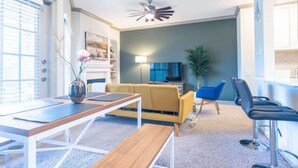 A modern living room with a sofa, a coffee table, a TV, and a ceiling fan. - Boulevard Stays Tranquil 1BR King Suite Pool, Parking Gym 04 (Austin)