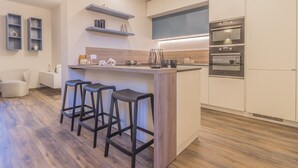 A modern kitchen with a central island, bar stools, built-in ovens, and wooden flooring. - Casa Lenora by Varenna Holidays (Bellano)