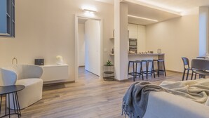 A modern living room with a sofa, a coffee table, and a dining area with a kitchen in the background. - Casa Lenora by Varenna Holidays (Bellano)