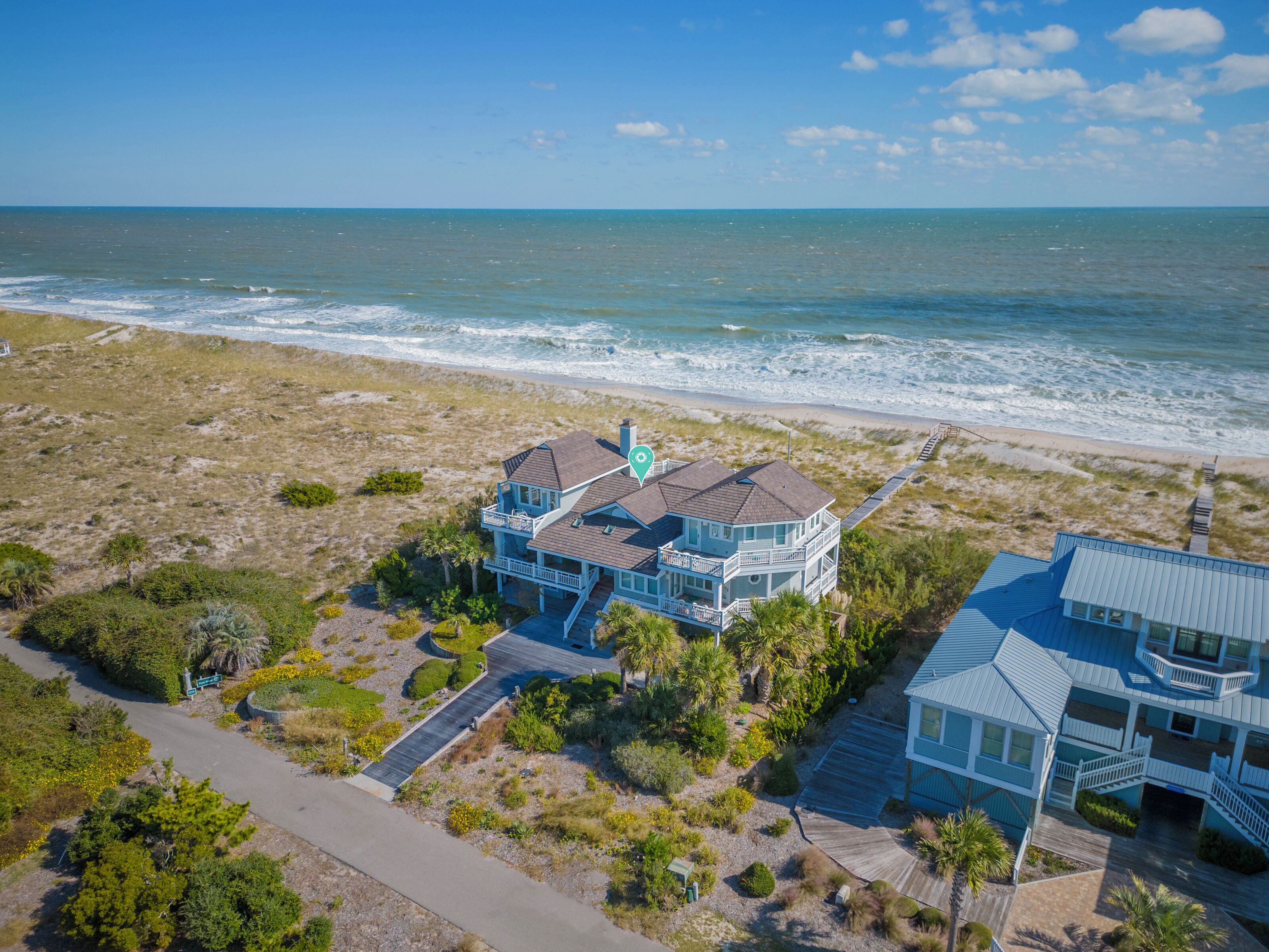 A coastal property with a large house featuring multiple balconies, a deck, and a view of the ocean.