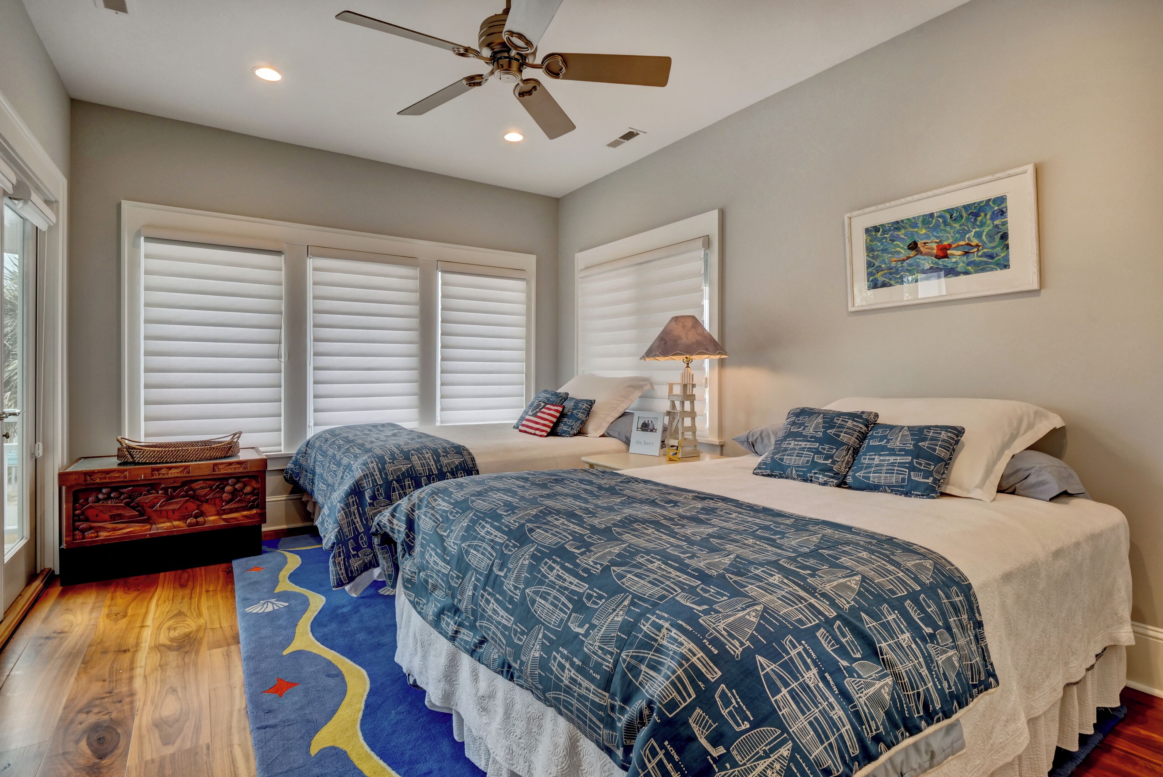 A bedroom with two beds, a ceiling fan, a framed artwork, and a window with blinds.