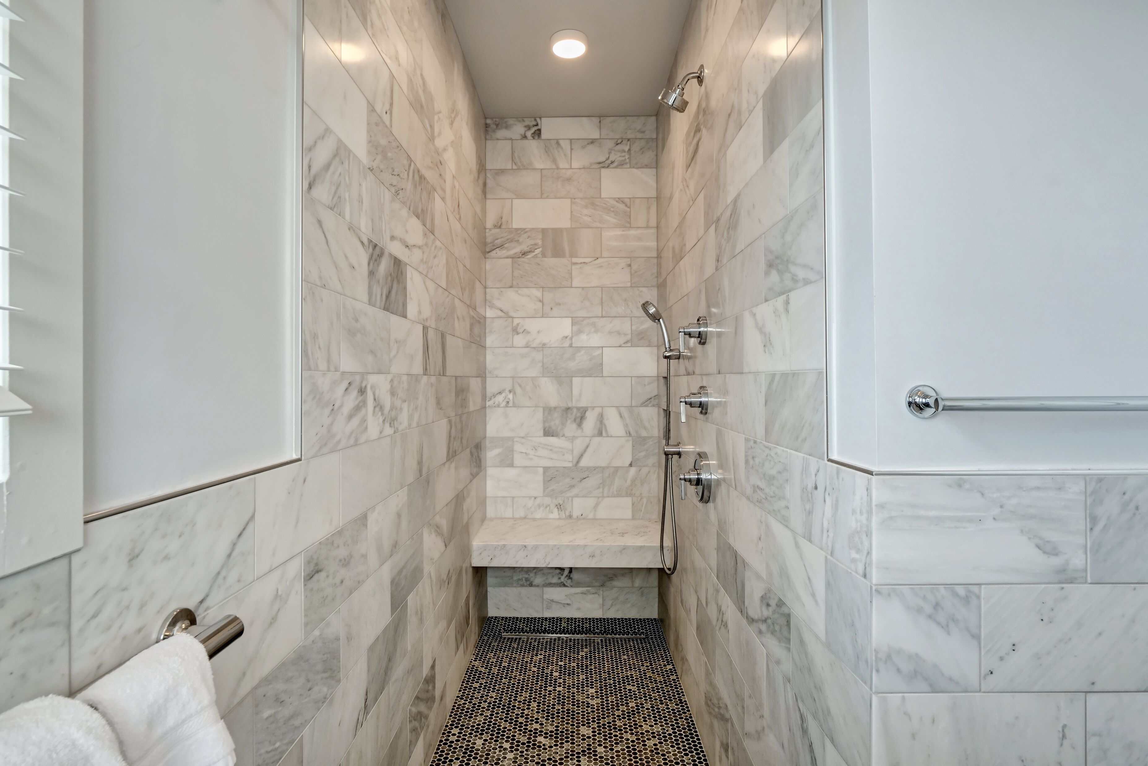Um chuveiro estreito com azulejos de mármore, um porta-toalhas e um chuveiro.