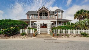 A two-story house with a balcony, a porch, and a white picket fence. - Five bedroom home on Bald Head Island's East Beach, make your next island getawa (Bald Head Island)