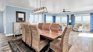 A dining room with a wooden table and wicker chairs, a ceiling fan, and a view of the ocean. - Incredible ocean views from Sand Castle on Bald Head Island (Bald Head Island)