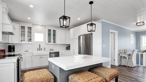A modern kitchen with white cabinets, a stainless steel refrigerator, and a central island with bar stools. - Incredible ocean views from Sand Castle on Bald Head Island (Bald Head Island)