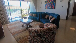 A living room with a blue sofa, patterned ottoman, and a coffee table. - PV 102 (Kibaoni)