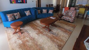 A living room with a blue sofa, patterned armchairs, a coffee table, and a colorful abstract painting on the wall. - PV 102 (Kibaoni)
