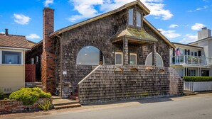 A rustic wooden building with a brick chimney, a porch with steps, and a small garden area. - 3965 Marine Gardens - Oceanfront with Bay Views (Pacific Grove)