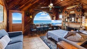 A cozy cabin with a wooden interior, a dining area with a view, a fireplace, and a large window overlooking the ocean. - 3965 Marine Gardens - Oceanfront with Bay Views (Pacific Grove)