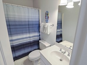 A bathroom with a striped shower curtain, a toilet, a sink with a mirror, and a towel rack. - Oceanfront Beach Cottage with Direct Beach Access (Bald Head Island)