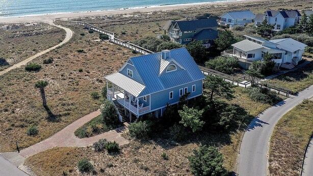 Een kustwoongebied met huizen met blauwe daken en witte muren, omgeven door een zandstrand en een helder uitzicht op de oceaan.
