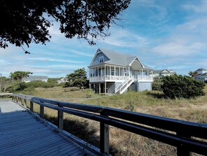 A coastal house with a wooden deck and a staircase leading to a porch. - Oceanfront Beach Cottage with Direct Beach Access (Bald Head Island)