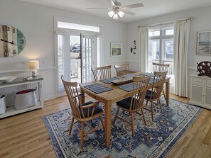 A dining area with a wooden table, chairs, and a patterned rug. - Oceanfront Beach Cottage with Direct Beach Access (Bald Head Island)
