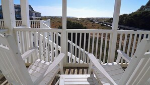 Een veranda met witte reling en twee witte Adirondack-stoelen, gericht op een strand en uitzicht op zee.