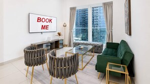 Un salon moderne comprenant un canapé, deux fauteuils, une table basse, un téléviseur fixé au mur et une grande fenêtre avec des rideaux.