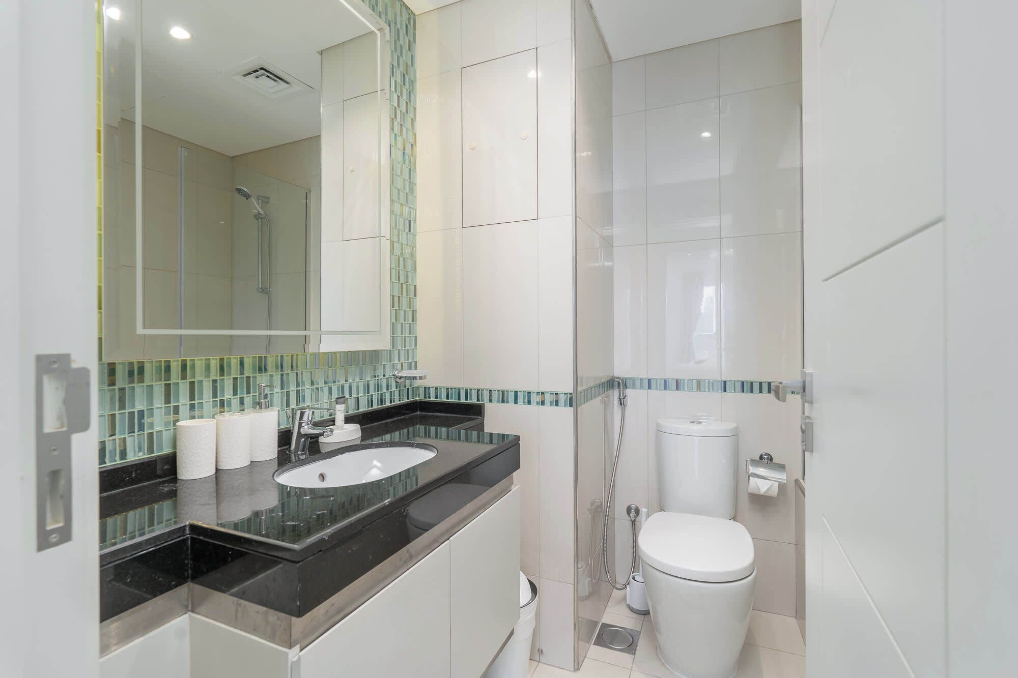 Une salle de bain moderne avec une douche à parois de verre, des toilettes blanches et un plan de toilette noir avec un lavabo.