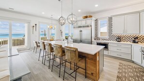 A modern kitchen with a large island, bar stools, and a view of the ocean.