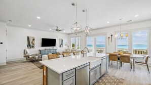 A spacious kitchen with a large island, a dining area with a view, and a living area with a TV and artwork.