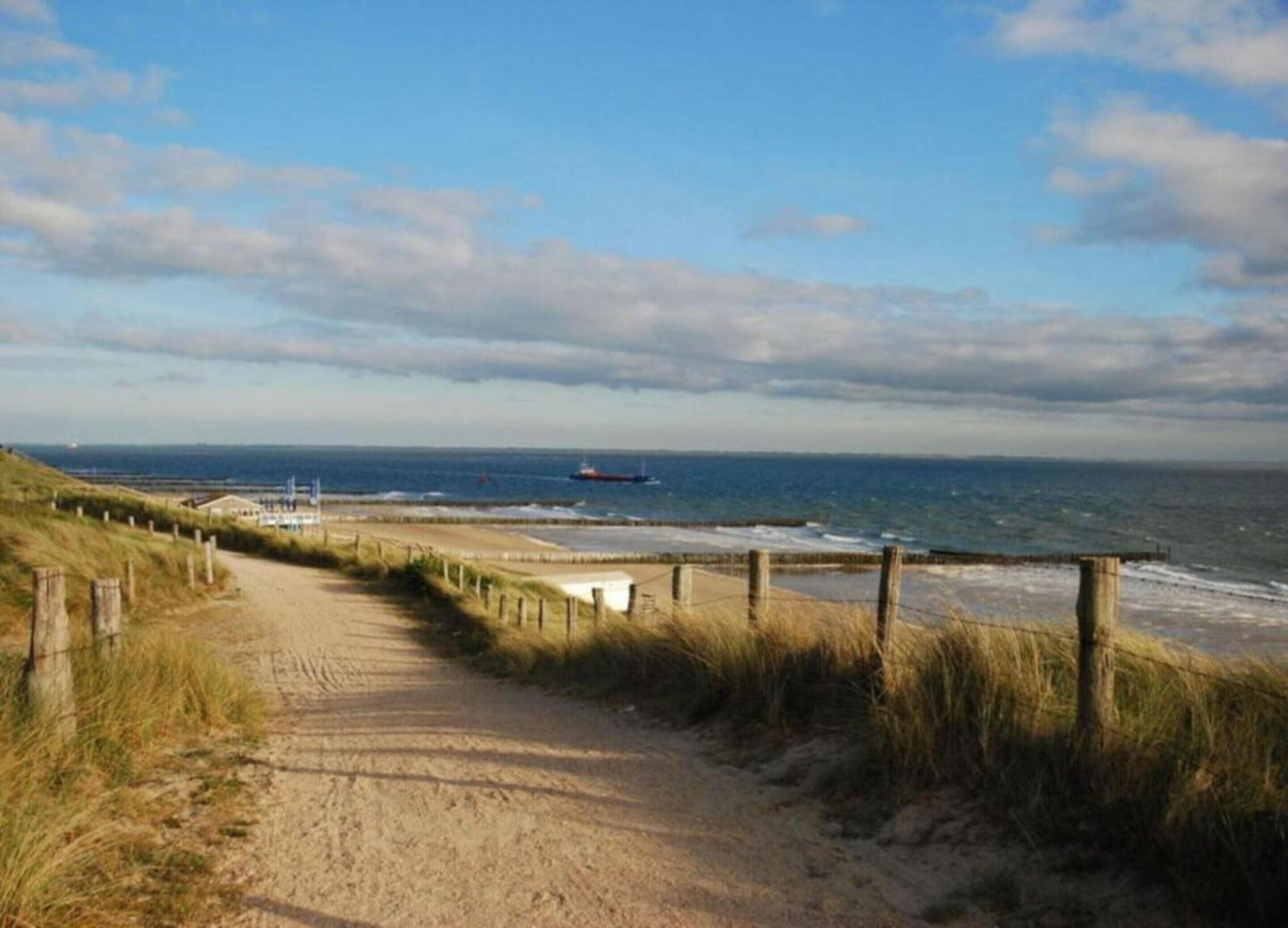 A coastal path leading to a beach with a sandy trail and wooden fencing.