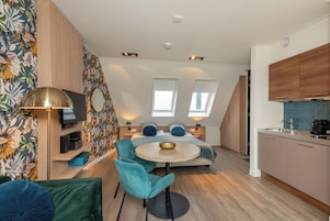 Une pièce de taille modeste comprenant un lit, une petite table, une chaise, un téléviseur et un coin cuisine.
