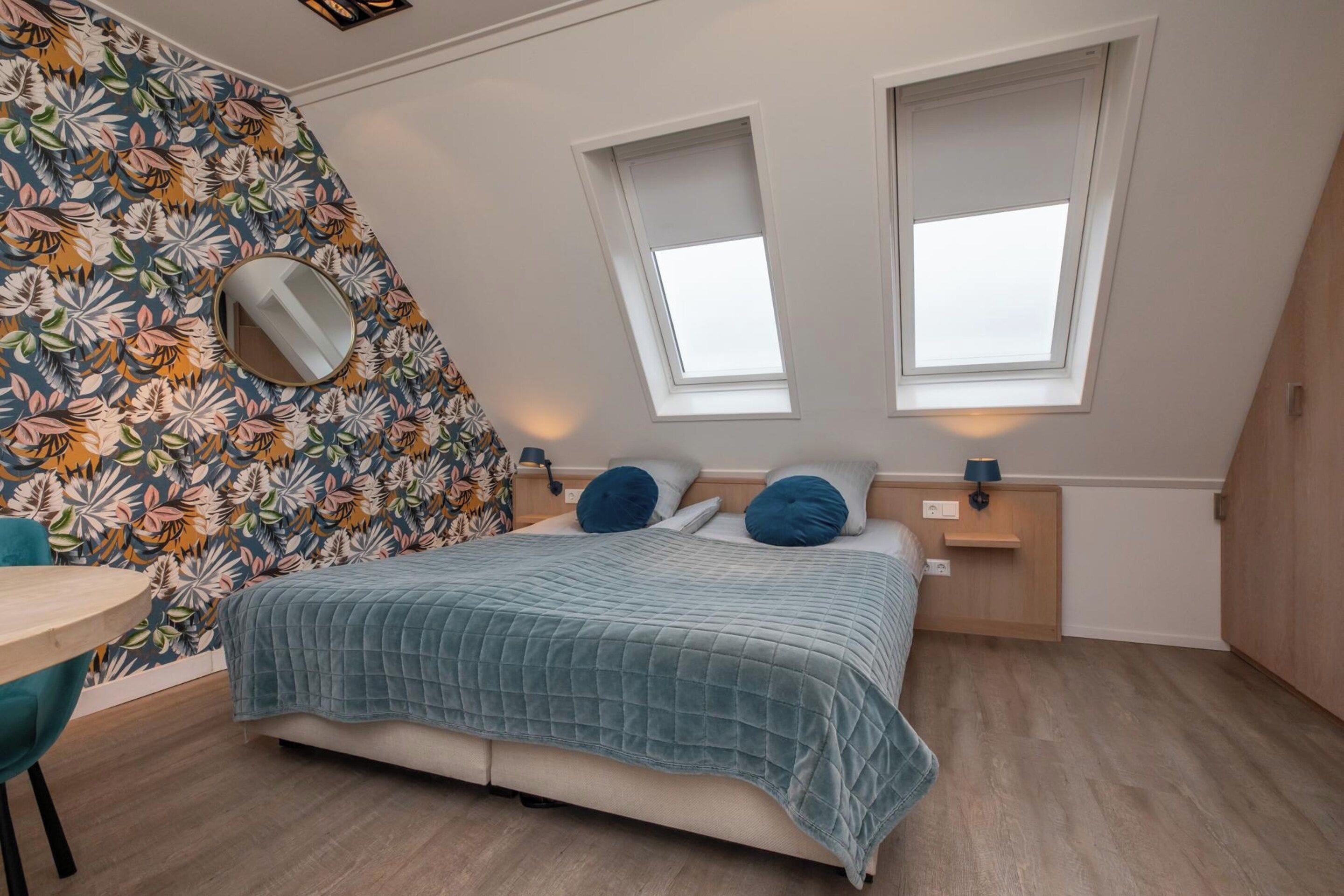 Een slaapkamer met een bed, twee nachtkastjes, een spiegel en een raam.