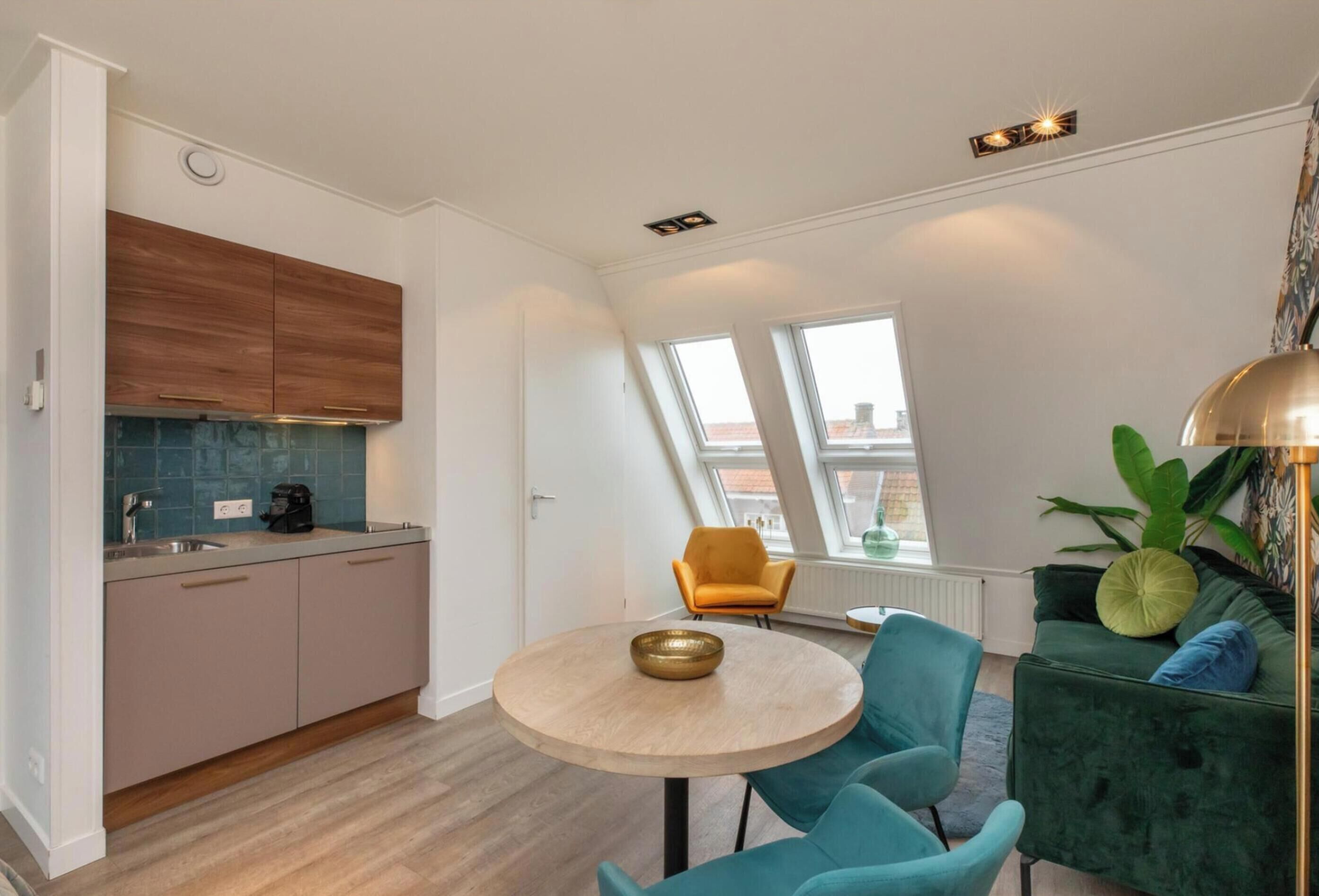 A modern kitchen with a round table, teal chairs, and a green sofa.