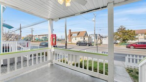 Un portico coperto con ringhiera bianca, una ventola a soffitto e vista su una strada con auto e case.