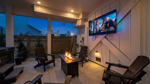 Eine Terrasse im Freien mit Feuerstelle, Sitzgelegenheiten und einem montierten Fernseher.
