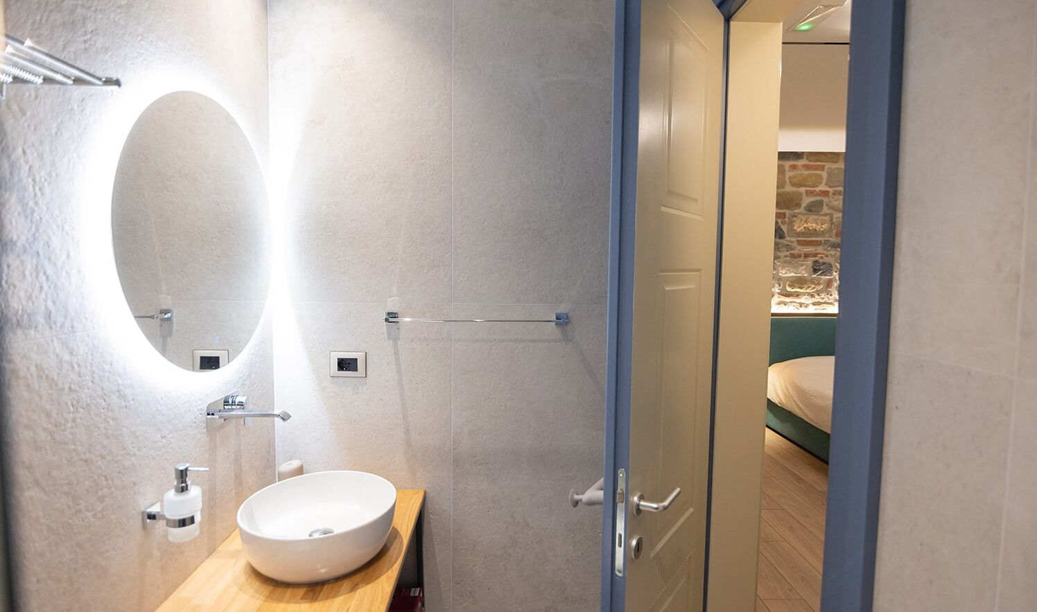Un baño moderno con un espejo ovalado grande, un lavamanos blanco y un perchero para toallas.