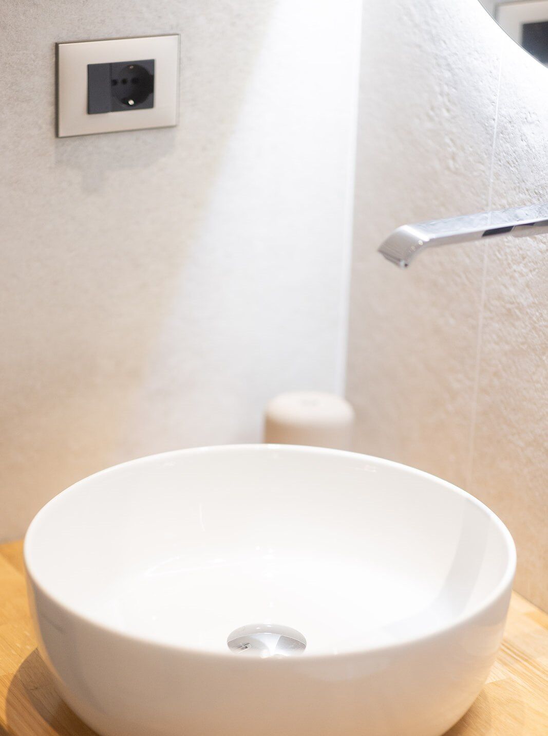 Un lavamanos blanco con un solo grifo, un enchufe en la pared y una pequeña botella de jabón.