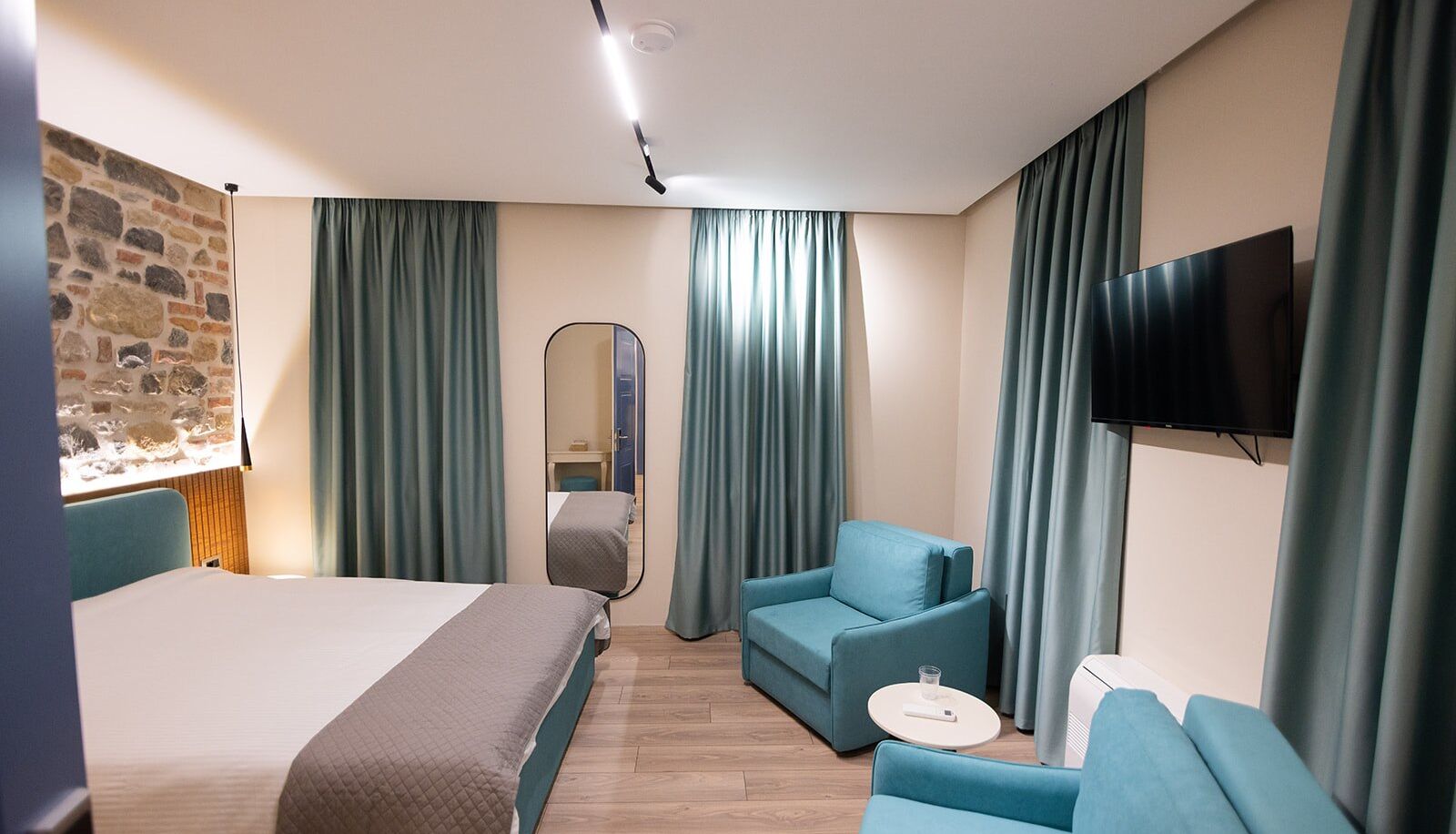 Une chambre d’hôtel avec un grand lit, un canapé, une petite table, une télévision et un miroir.