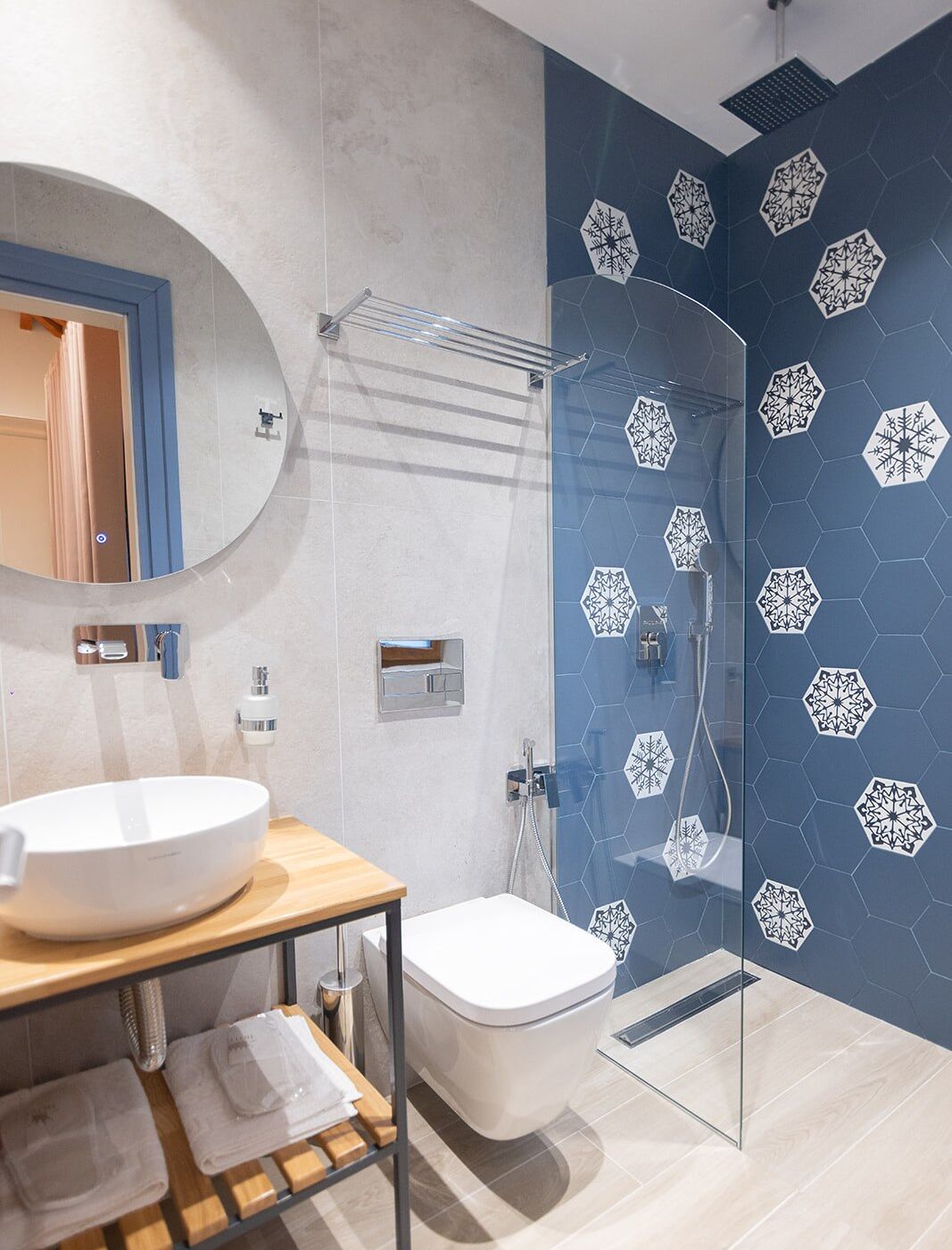 Un baño moderno con un lavamanos grande y blanco, un inodoro y una ducha envuelta en vidrio con pared de azulejos hexagonales azules.