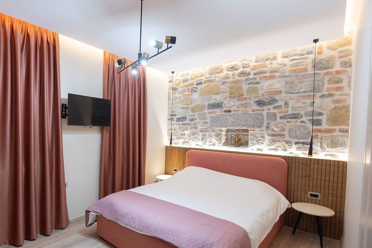 Un dormitorio con pared de piedra, cama, televisor y cortinas.
