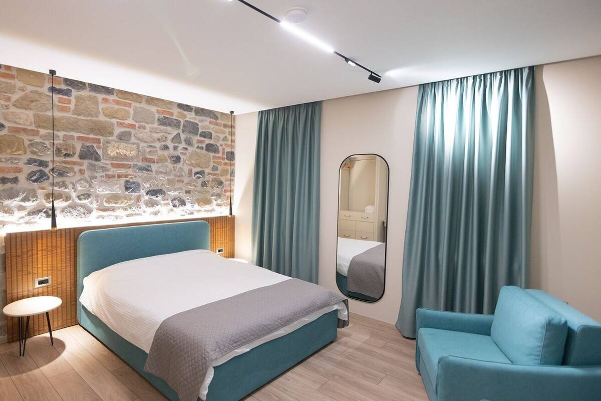 Un dormitorio moderno con pared de piedra, una cama, una silla y un espejo.