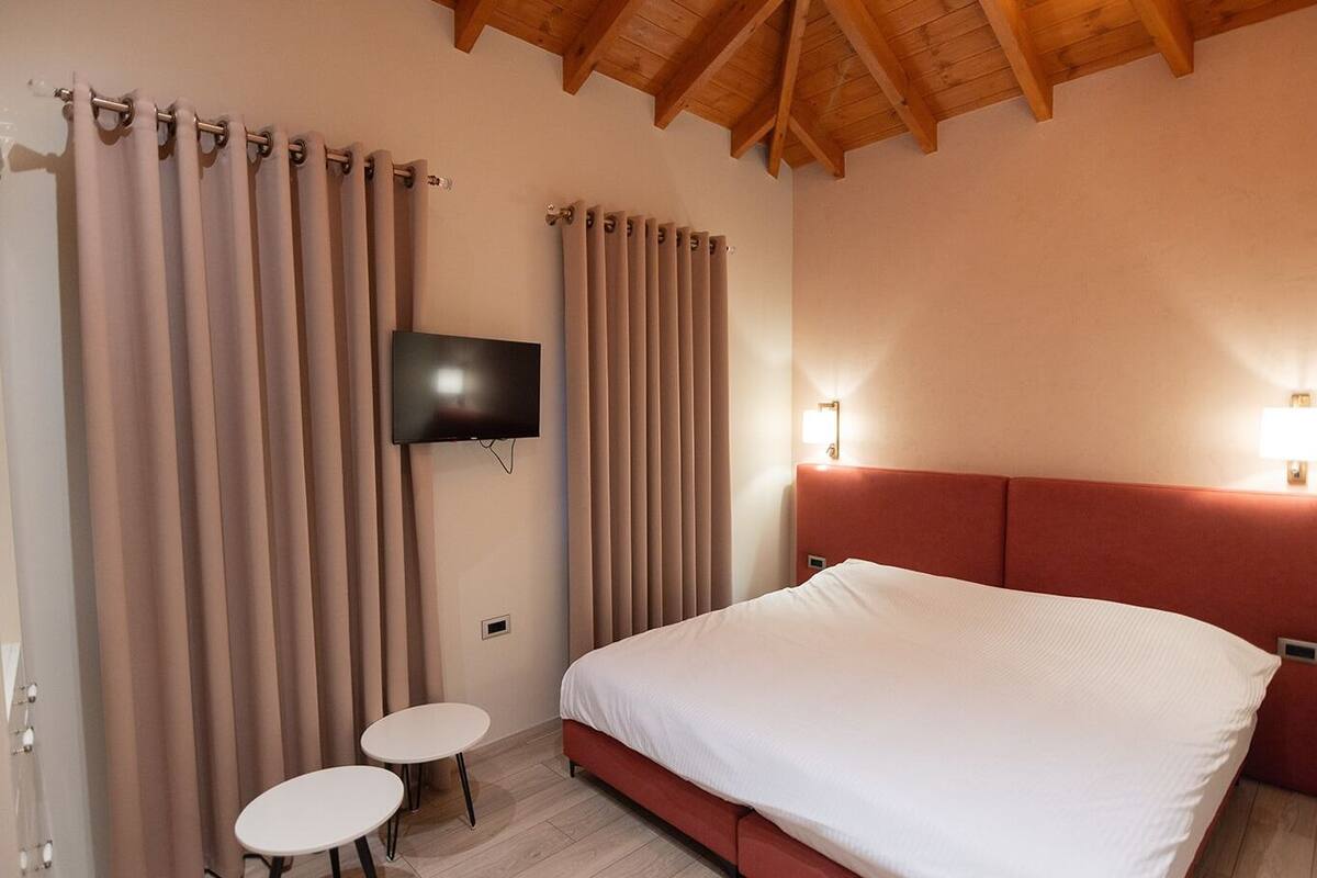 Una habitación de hotel con cama, televisión, dos mesitas de noche y cortinas.